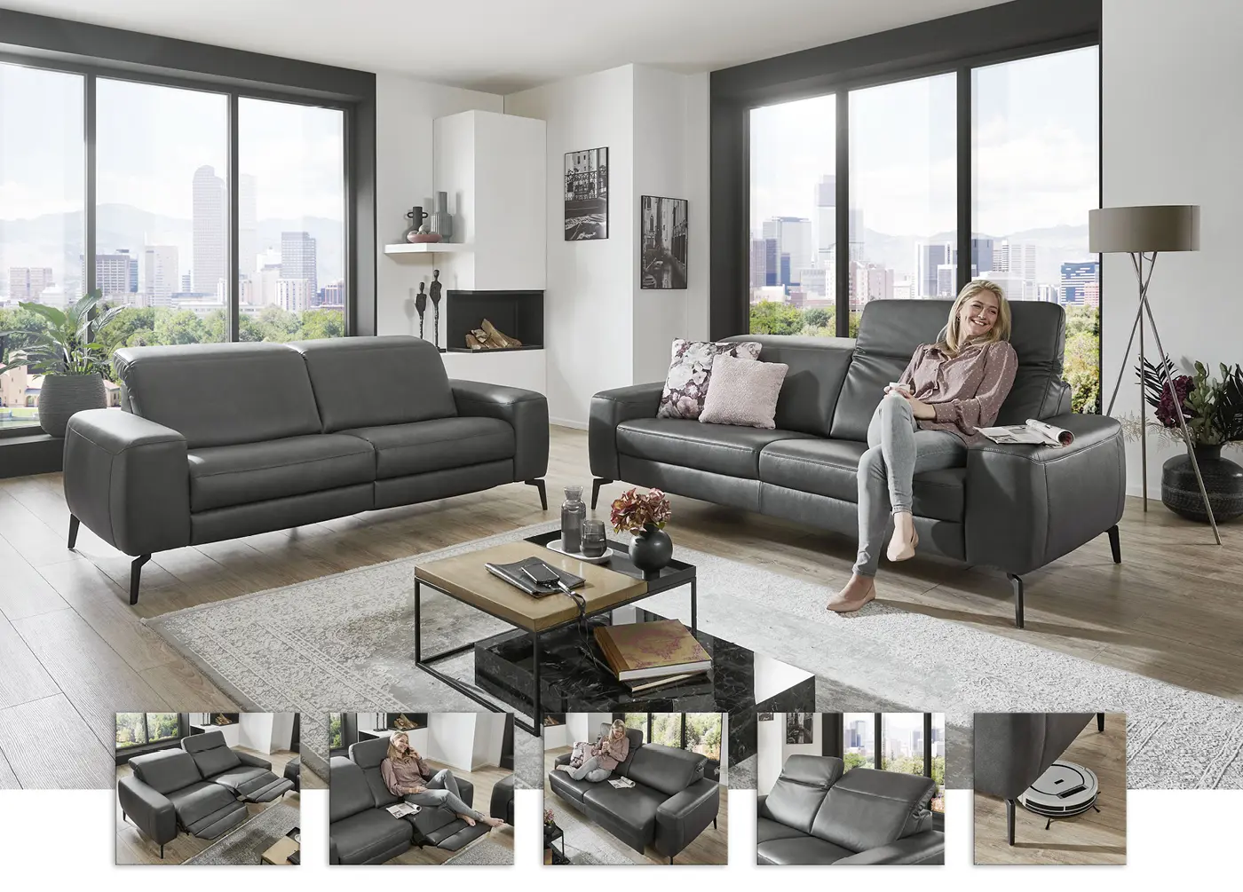 Modernes Wohnzimmer mit zwei grauen Ledersofas auf schwarzen Metallfüßen. Frau sitzt entspannt auf einem Sofa, großer Teppich und Couchtisch im Mittelpunkt, bodentiefe Fenster mit Stadtblick und Kamin sorgen für stilvolles Ambiente.